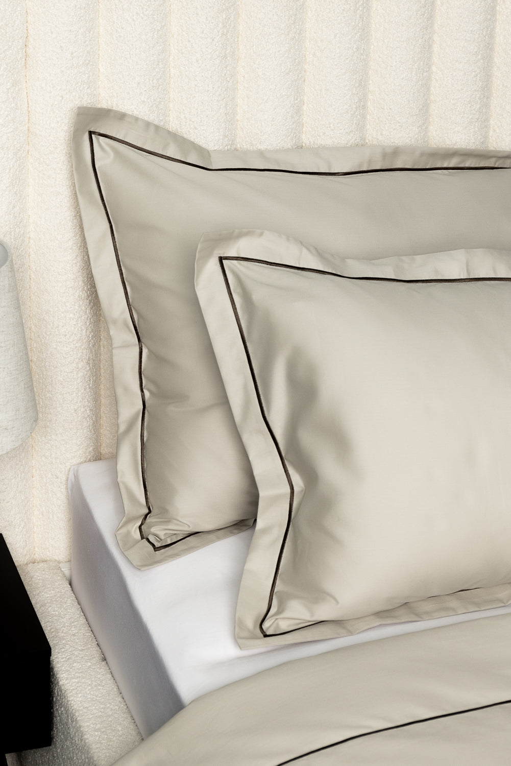 Beige satin pillows with black piping on a bed.