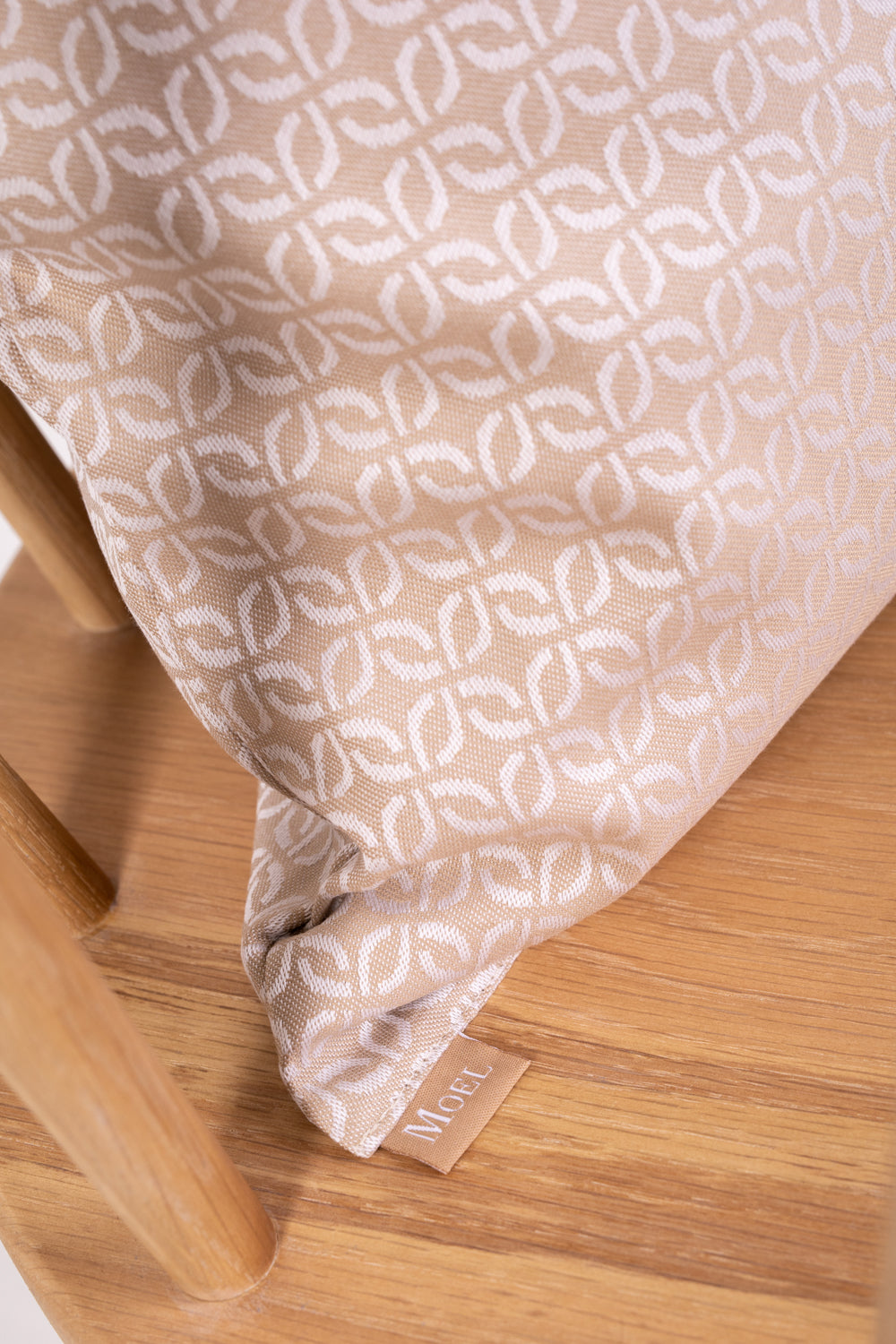 A beige cushion with a clover pattern on a wooden chair with no one sitting