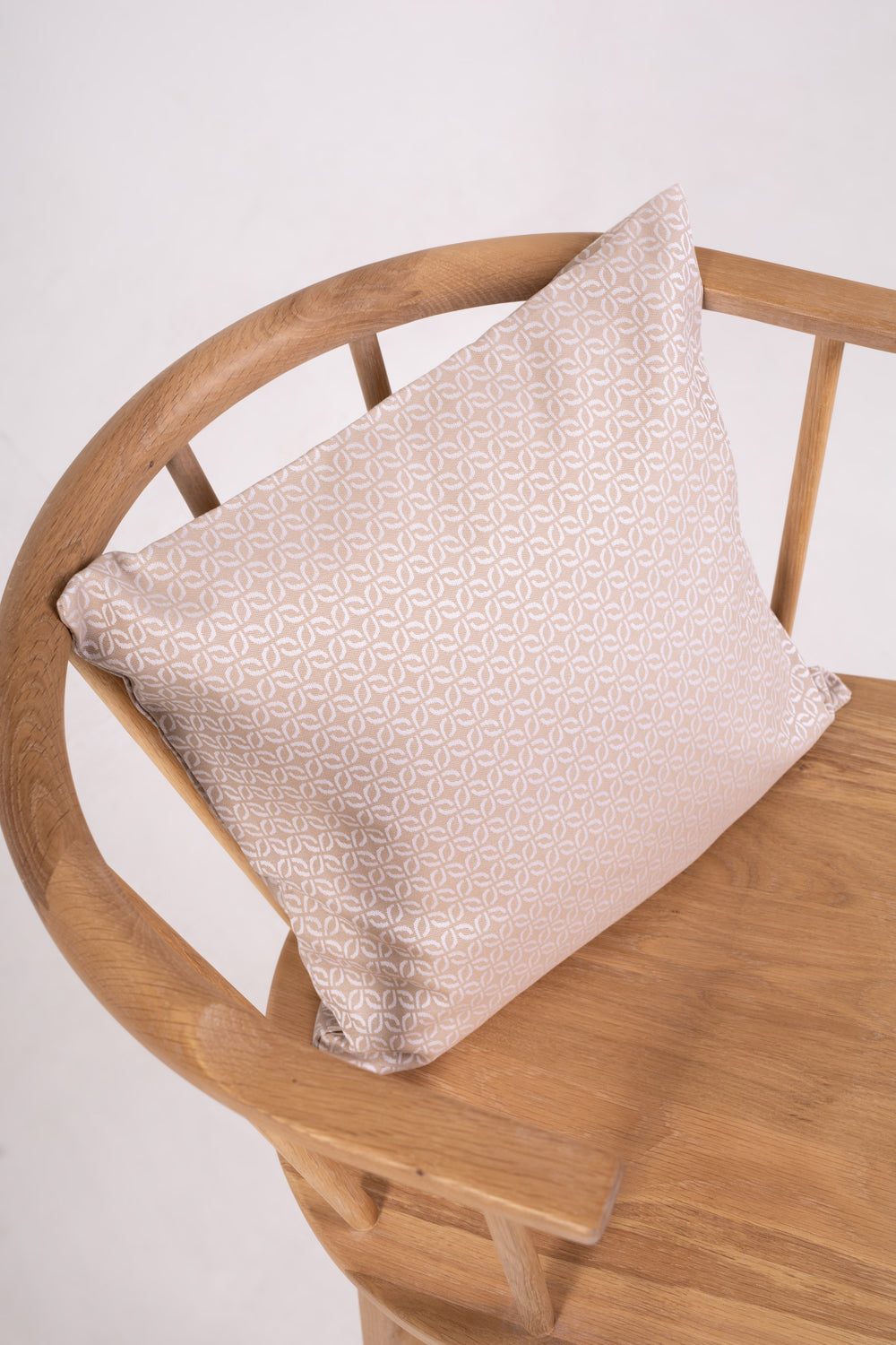 A beige cushion with a clover pattern on a wooden chair with no one sitting