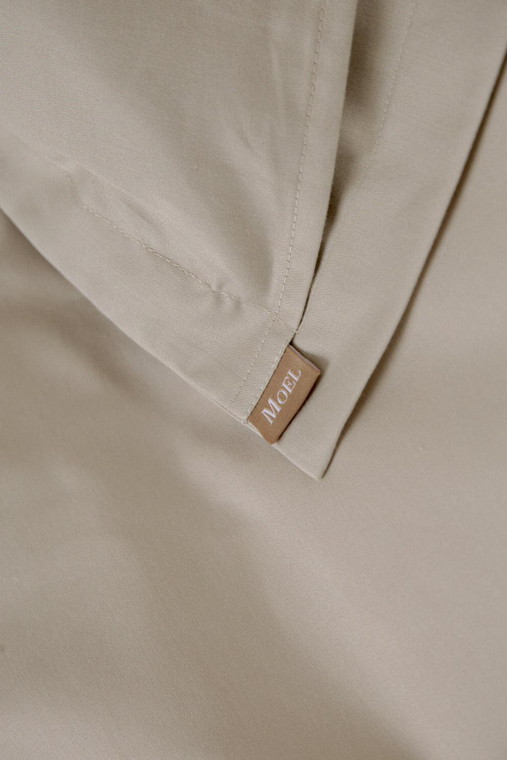 Close-up of beige fabric with a brand label on a neutral background