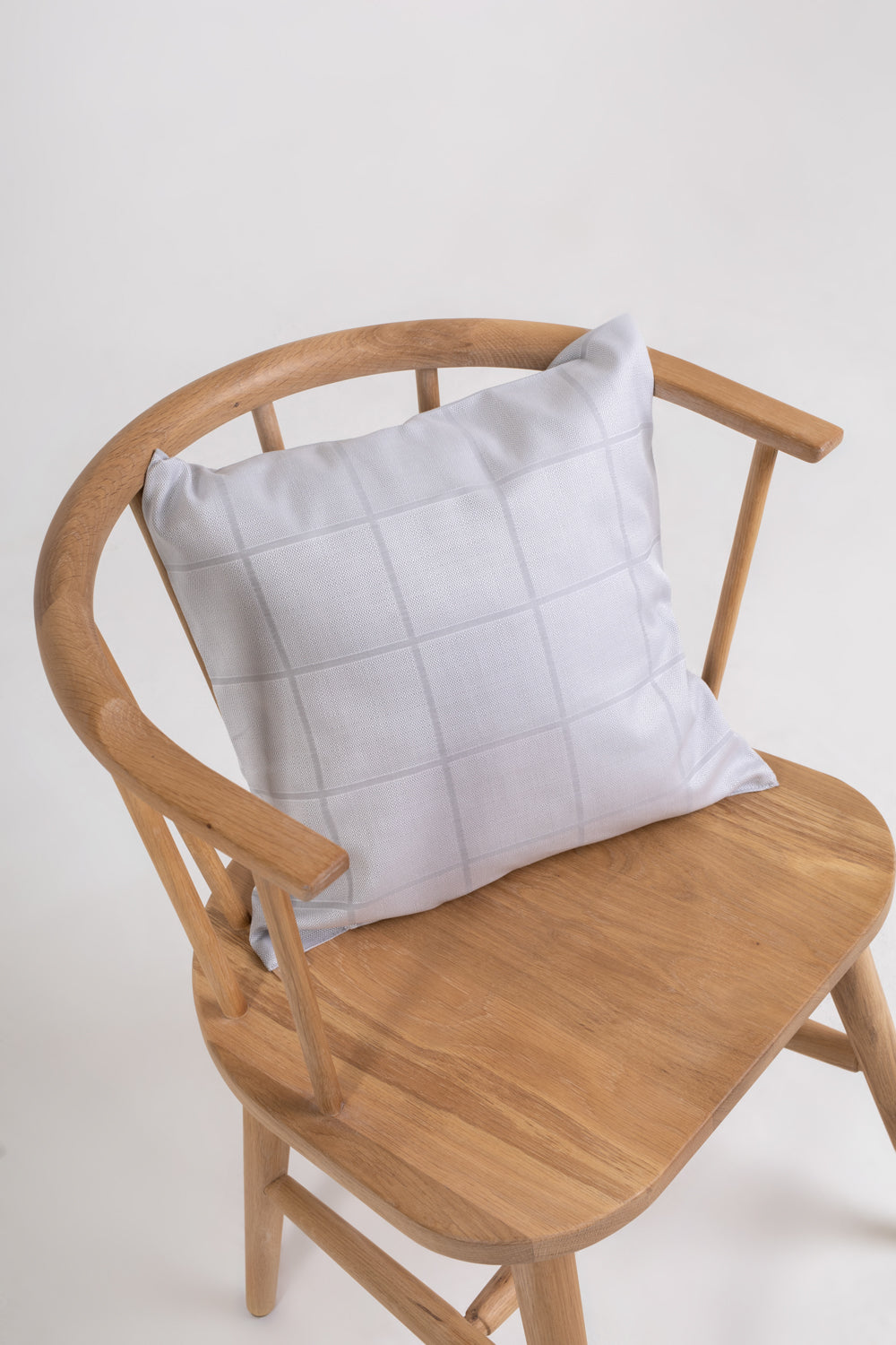 A square-shaped throw pillow with a gray damask pattern, placed on a wooden chair.