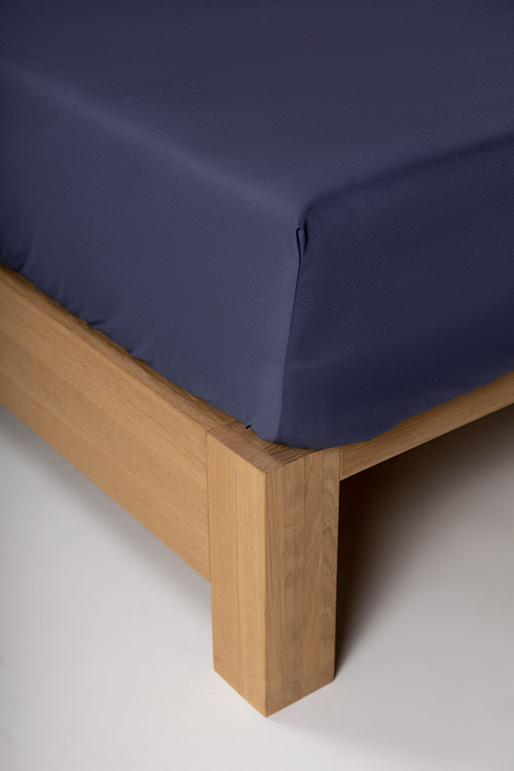A navy blue fitted sheet on a bed, showcasing the corner detail with a wooden bed frame.