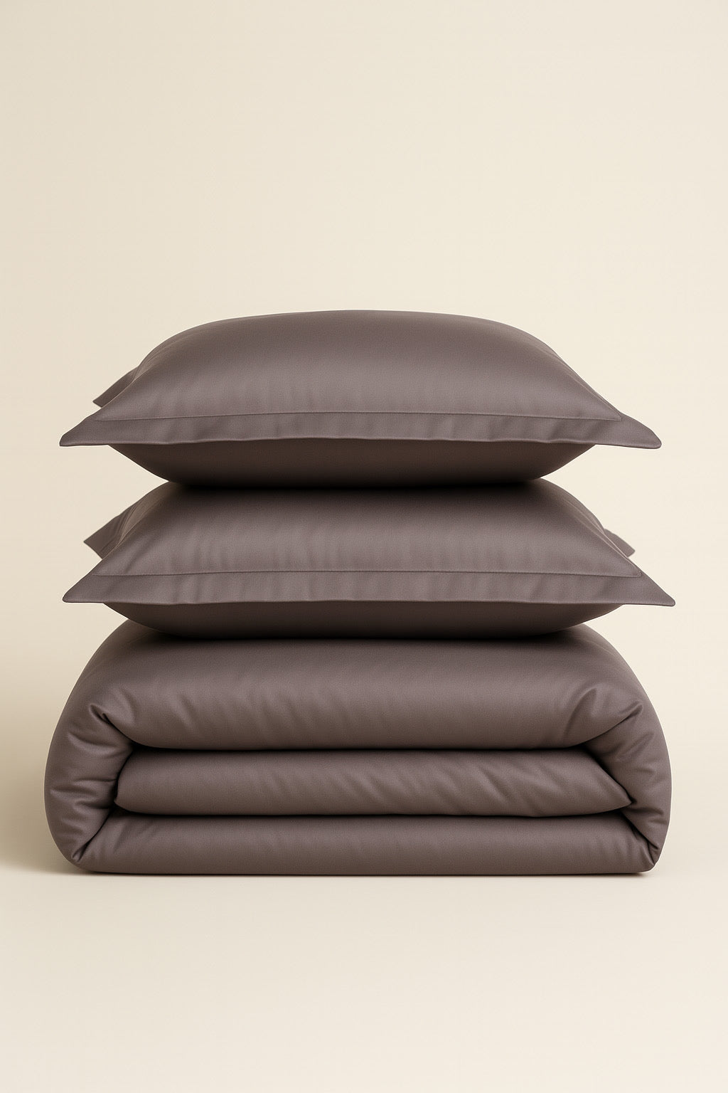 Stack of brown bedding including a duvet and two pillows on a beige background