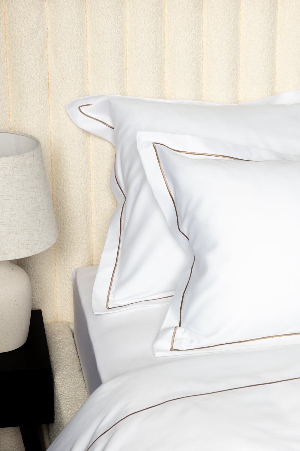 White bed linens with gold trim on a bed in a bedroom setting.