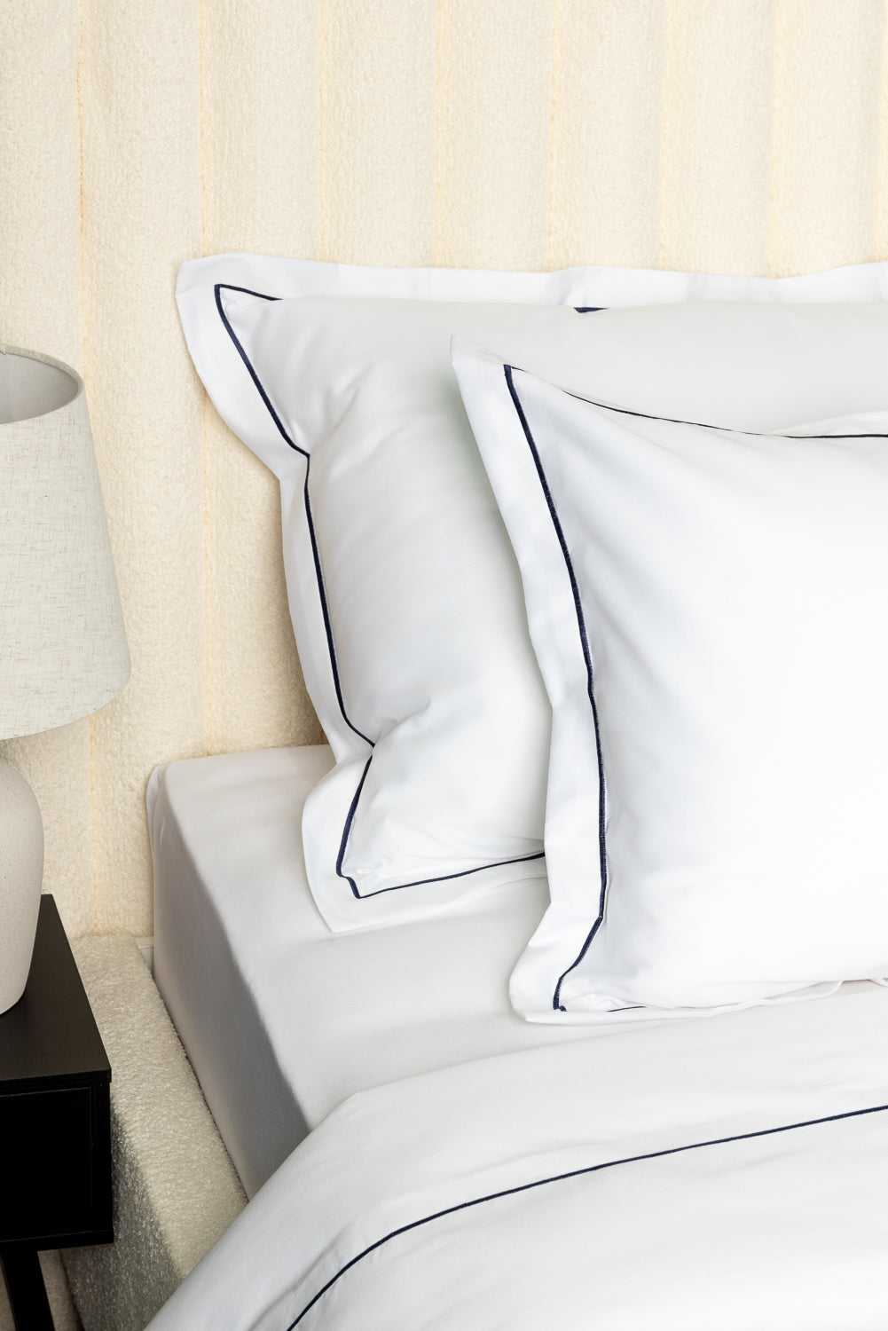 White bedding with navy blue piping on a bed against a beige wall.